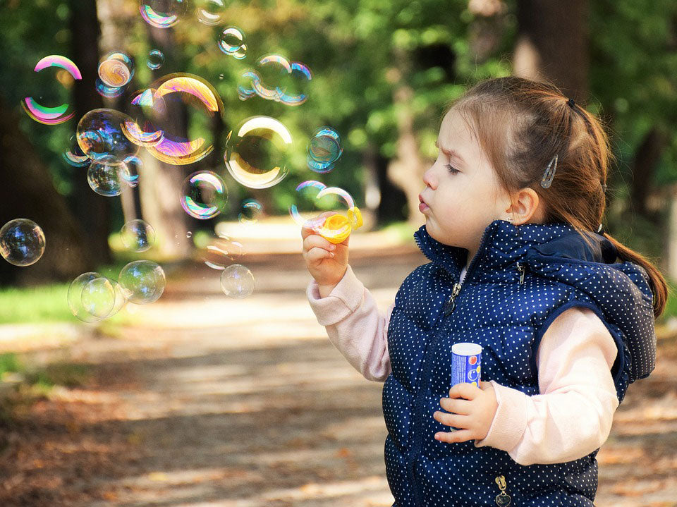 Small girl blows bubbles in park