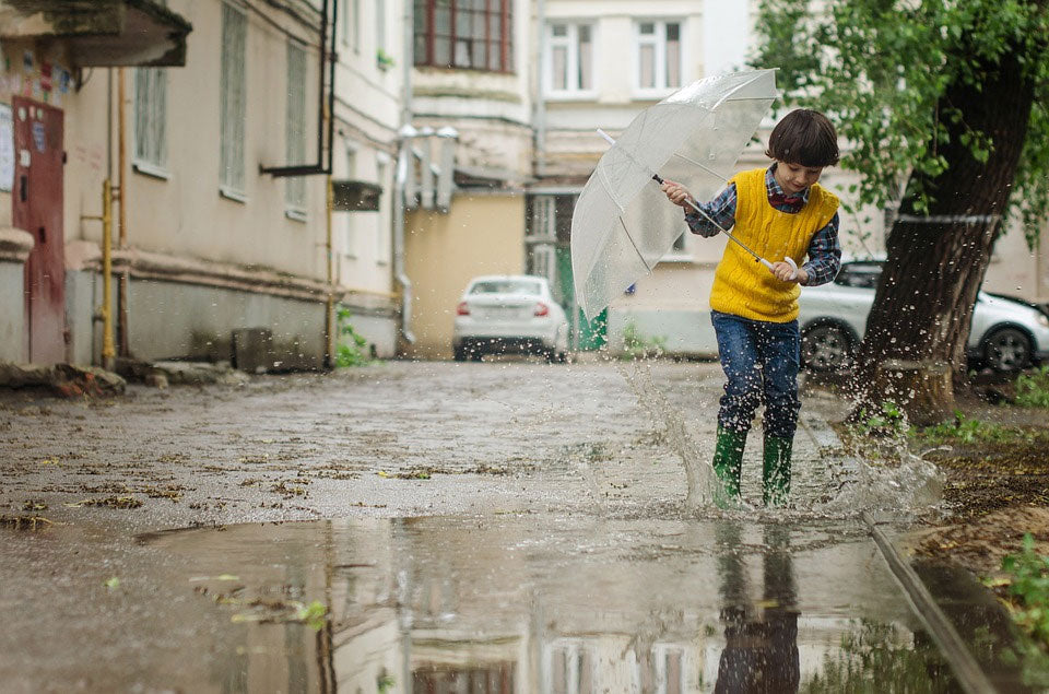 Little boy splashes in rain puddle on the street