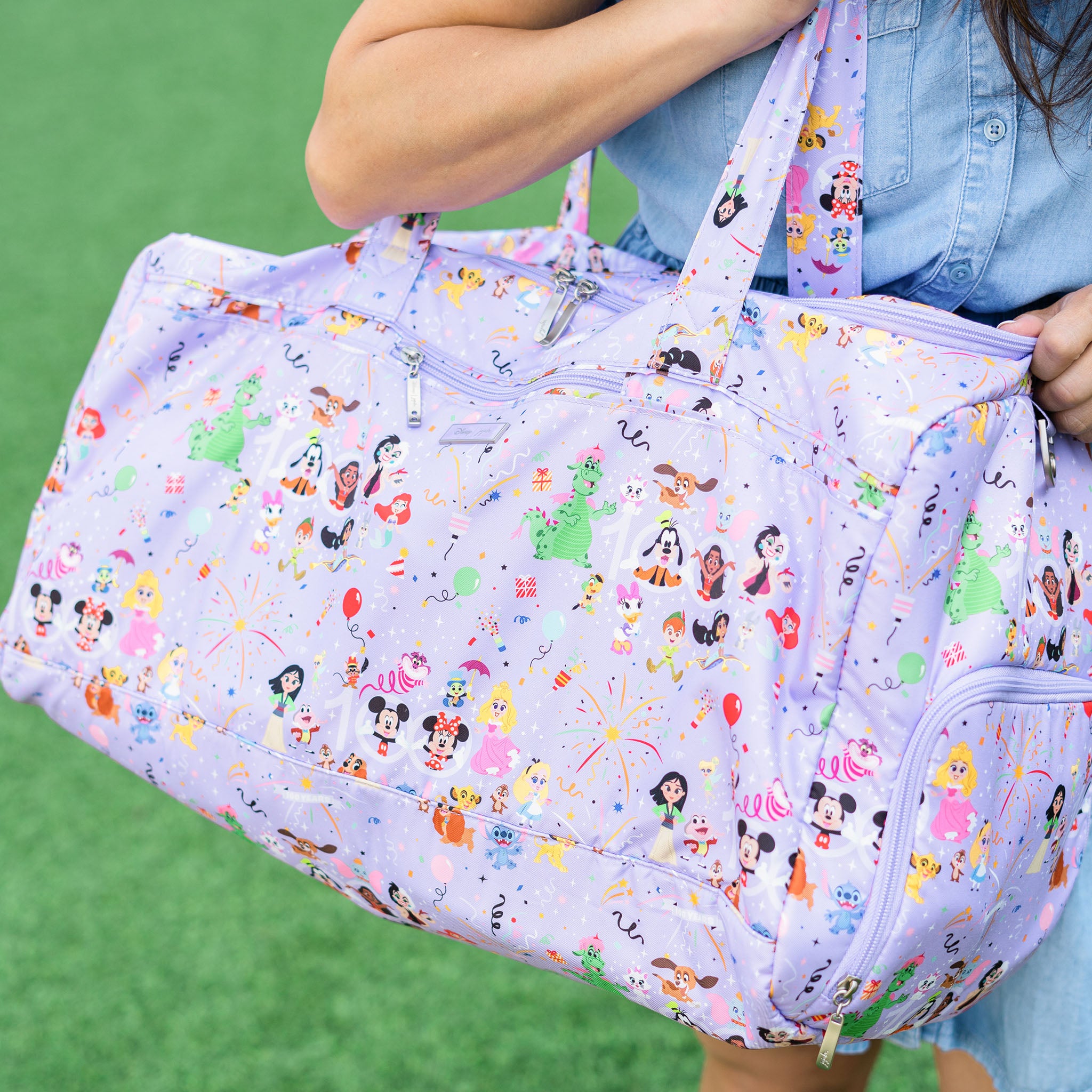 A purple duffel bag with a D100 Disney's Century of Magic print, showcasing beloved Disney characters from the past century. The design pays homage to Disney's rich history, encompassing a variety of iconic characters that have captured the hearts of audiences over the last 100 years.