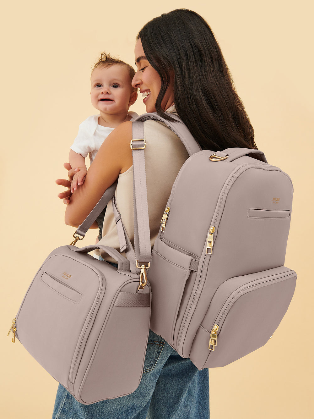 Parent wearing the JuJuBe Classic Diaper Backpack in Taupe while carrying a baby