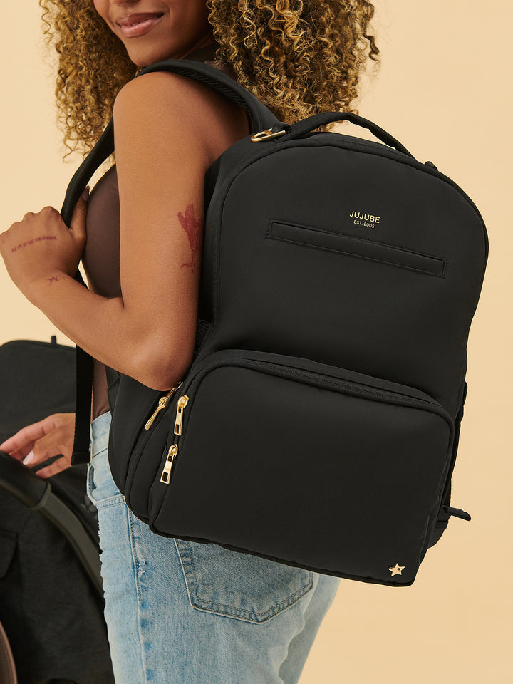 Parent carrying the JuJuBe Classic Diaper Backpack in Black 
