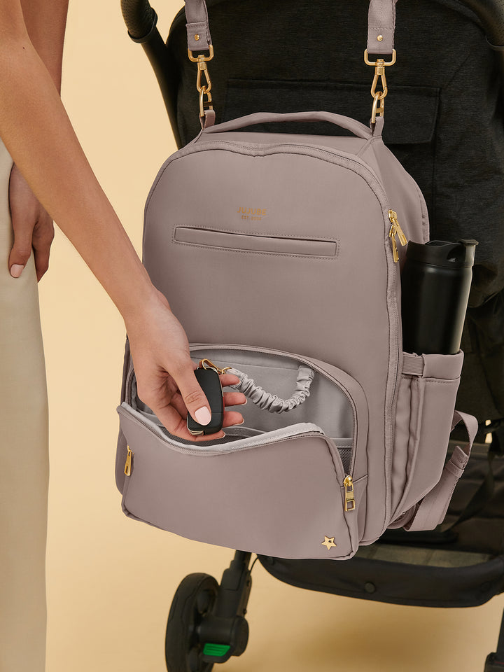 Parent pushing a stroller with the JuJuBe Classic Diaper Backpack in Taupe secured to the handlebar