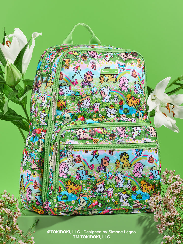 tokidoki x JuJuBe Zealous Diaper Bag Backpack in Meadow Blooms – front view of the backpack styled in a lush green garden setting