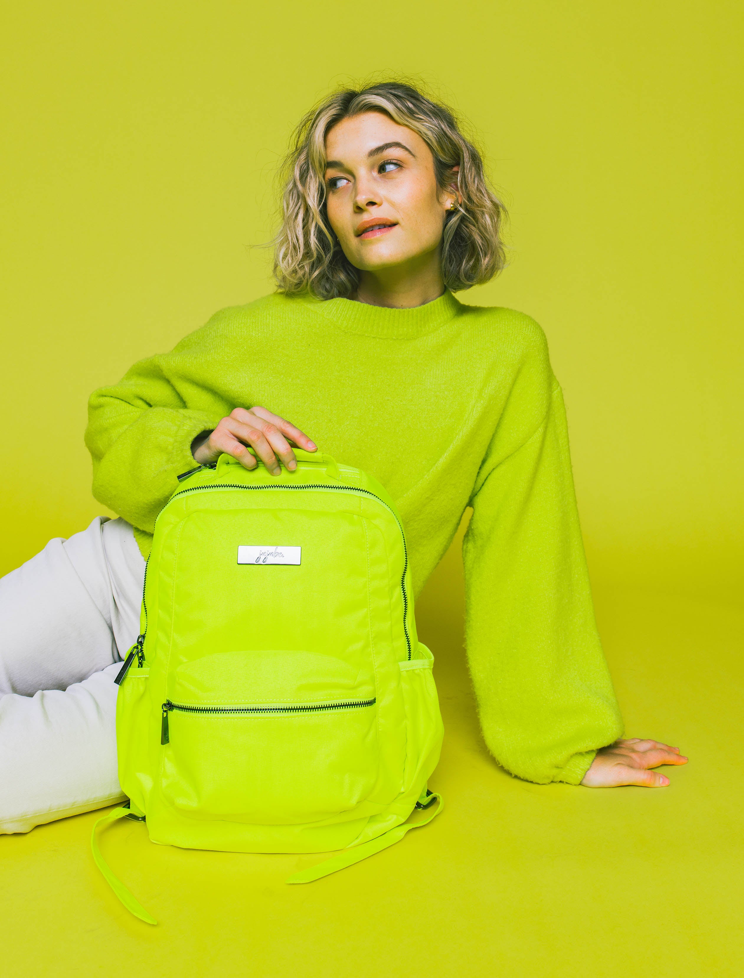Neon Yellow Be Packed Backpack sitting in front of woman wearing matching colored sweater