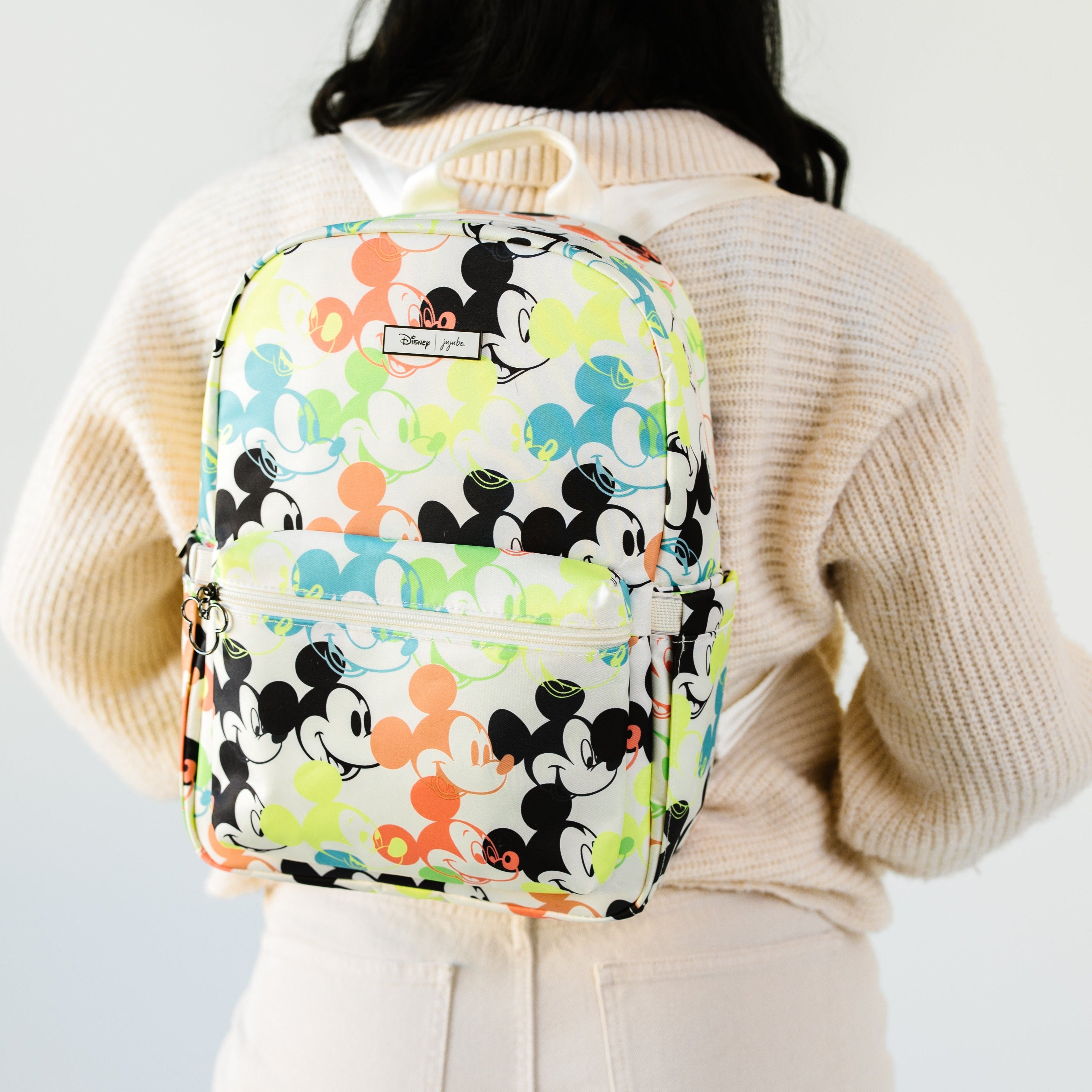 Lifestyle shot of a cream white background displaying a multicolored Pop Art design of Disney's Mickey Mouse; Diaper Backpack